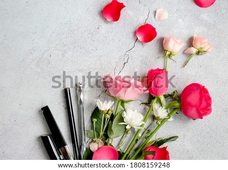 flat photo of light grey background with beauty items, rose petals, cosmetics, mobile phone and space for text on the picture. 
Women's fashion. A stylish life. Makeup tools and pink flowers 