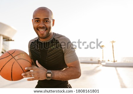 Image of cheerful african american sportsman smiling while playing basketball outdoors