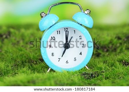 Blue alarm clock on grass on natural background