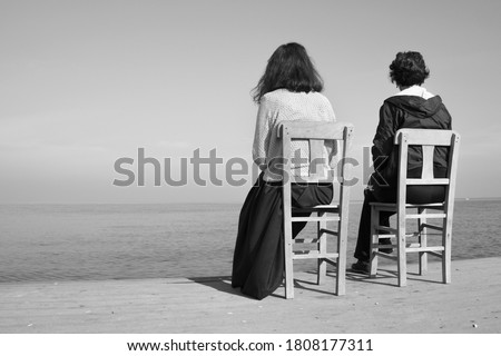 Mother and daughter sitting on chair on pier. Different generations concept photo. Selective focus on chairs and people.