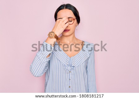 Young beautiful woman wearing casual striped shirt and glasses over pink background tired rubbing nose and eyes feeling fatigue and headache. Stress and frustration concept.
