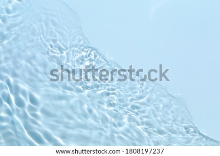 Blurred transparent blue colored clear calm water surface texture with splashes and bubbles. Trendy abstract nature background. Water waves in sunlight with copy space.