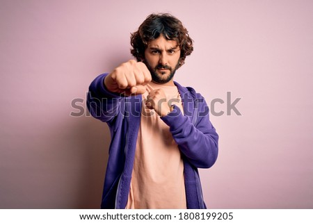 Young handsome sporty man with beard wearing casual sweatshirt over pink background Punching fist to fight, aggressive and angry attack, threat and violence