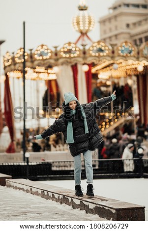 Cute girl near the Christmas carousel. Smiling young beautiful  woman in the middle of decorated old town European Christmas square near the carousel.