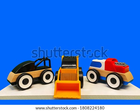 Three toy multicolored cars made of plastic and wood on a blue background