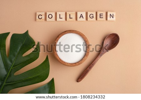 collagen powder in a wooden bowl, spoon, peach background, top view, green leaf, lettering Royalty-Free Stock Photo #1808234332