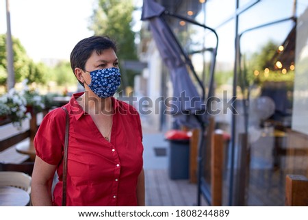 Beautiful European woman with dark hair wearing handmade protective mask in cafe
