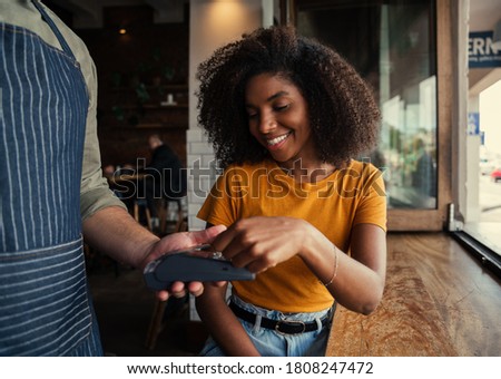 Smiling mixed race woman with afro happily paying for coffee at coffee shop.