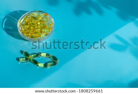 Gelatin transparent capsules with fish oil in a glass bowl on a blue background. Horizontal orientation, selective focus, copy space.