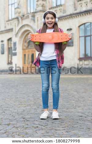 Happy small child hold penny board listening to music in headphones sumer outdoors, skateboard.