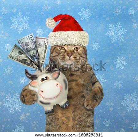 A beige cat in a Santa Claus hat holds a money box cow. Snow blue background.
