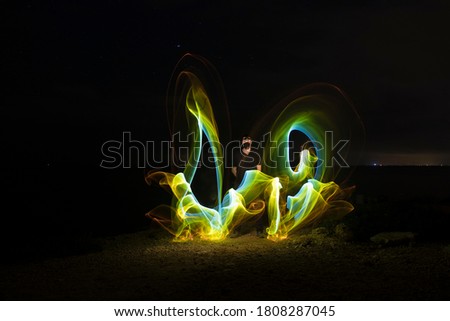 Lightpainting of a man posing with a mask and colorful light next to him