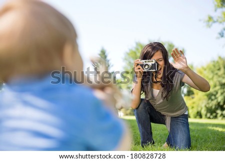 Happy young mother photographing son through camera in park