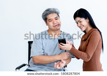 Asian husband Who is patient from nervous system and paralysis or hemiplegia, watching applications on a mobile phone, Which his attractive wife are holding On white background. Royalty-Free Stock Photo #1808287804