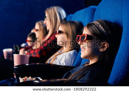 Selective focus of laughing child wearing 3d glasses, eating popcorn and watching funny movie. Cute little girl enjoying time with friends in cinema. Concept of leisure and entertainment.
