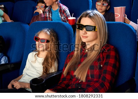 Happy family spending time together in cinema. Attractive young mother and laughing little daughter wearing 3d eyeglasses while watching film. Concept of leisure, entertainment.