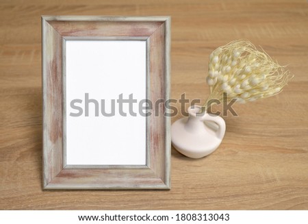 Mockup poster wooden frame with white clay vase with dry artificial plant on wooden background.