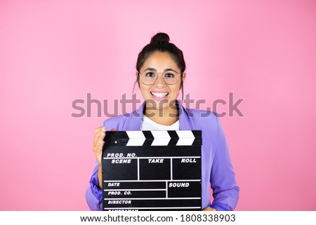 Young beautiful business woman over isolated pink background holding clapperboard very happy