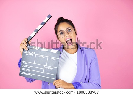 Young beautiful business woman over isolated pink background holding clapperboard very happy having fun