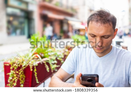 Young man sitting at table in European outdoor cafe restaurant looking down at phone in summer in Lviv or Lvov, Ukraine city
