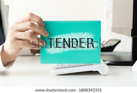 Sticker with text Tender on a white paper holding by a man in suit. Unfocused background