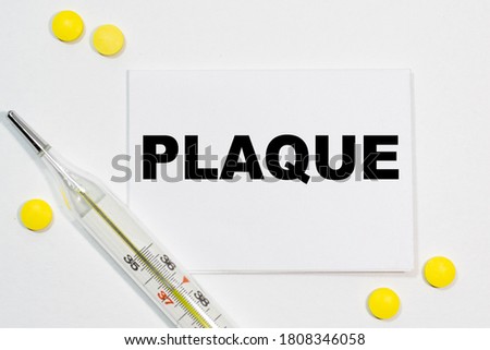 PLAQUE text written on a white business card next to yellow tablets and a thermometer. Medical concept.