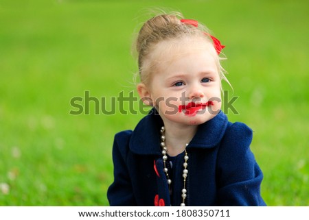 the child sits and paints his lips with red lipstick