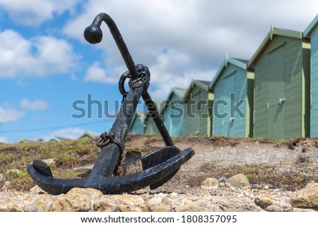 Photo of the anchor at Charmouth beach with beach huts in the background