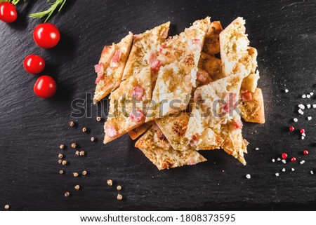 Traditional Italian focaccia among tomato and spices on a dark background, studio light. Traditional food concept