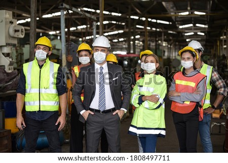 Group of industrial staff worker consist of Technicians, Engineers and factory Manager wearing helmet or hardhat with surgical mask to protect Covid 19 inflection outbreak in Industry plant/Teamwork