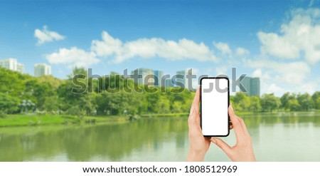 Business Communication Concept : Hand holding black smartphone with white blank screen and blurred cityscape park view with blue sky in background.