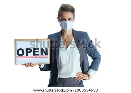 Business during covid-19 pandemic. Portrait of middle aged business woman in a grey suit with medical mask showing open sign against white background.