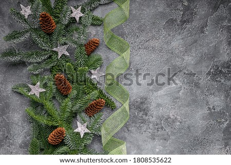 Border of green spruce branches with Christmas decorations: stars and cones on a gray-blue background. Christmas or New Years blank. Copy space