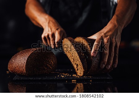 Man cutting whole grain bread on a stone board, dark background 