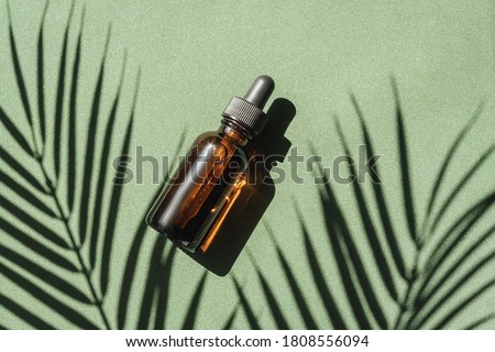 top view of Blank amber glass essential oil bottle with pipette on green background with tropical leaves shadows. Royalty-Free Stock Photo #1808556094