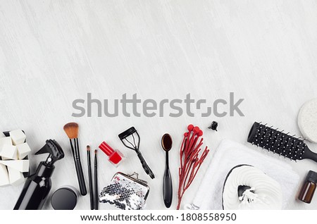Black beauty products, accessories for makeup, manicure - brushes, sponges, buds, pads, towel, red nail polish, cream, beautician on white wood board.