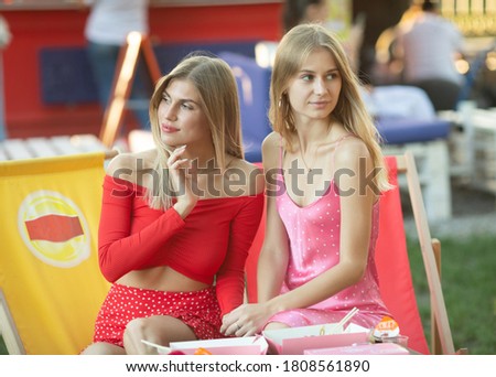 Two attractive young girl friends standing together and posing on camera.