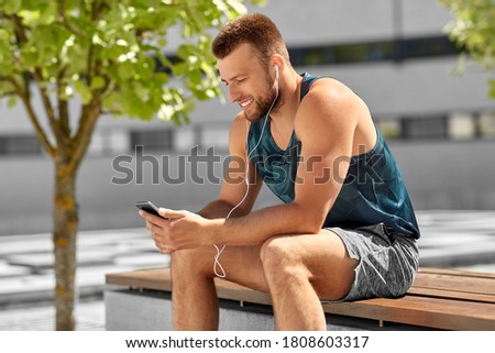fitness, sport and technology concept - young athlete man with earphones and smartphone listening to music outdoors