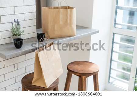 Mock-up of big brown paper package with handles, blank craft shopping bag with area for your logo or design, white wall in the background, food delivery concept