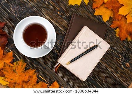 Notebook diary Cup of tea on a pile of bright autumn leaves against a dark wooden table. Top view, Flatley. Hugge and comfort in the house