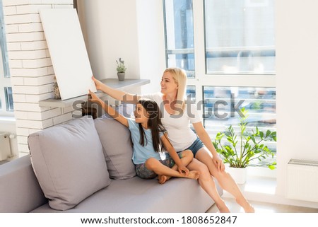 mother and daughter hangs a large photo canvas at home
