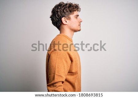Young blond handsome man with curly hair wearing casual sweater over white background looking to side, relax profile pose with natural face and confident smile. Royalty-Free Stock Photo #1808693815