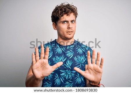 Young blond handsome man on vacation with curly hair wearing casual summer t-shirt Moving away hands palms showing refusal and denial with afraid and disgusting expression. Stop and forbidden.
