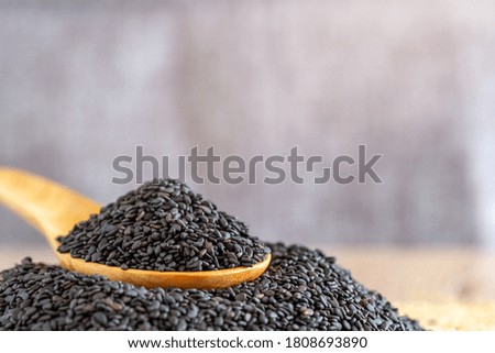 Black dried sesame seed on wooden spoon over wood table.
