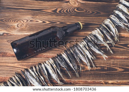 Small dry fish on a rope on a wooden background and brown beer bottle. Studio photo.