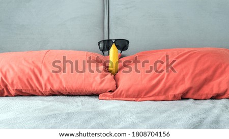 Banana with glasses in the apartment on the bed in the bedroom, red pillows,funny banana with glasses.