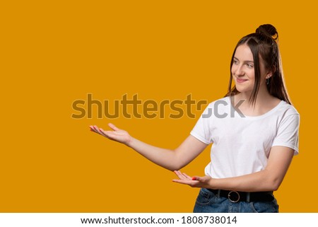 Welcome gesture. Inviting sign. Happy young girl pointing aside. Isolated on orange copy space. Text message. Education courses. Advertising background