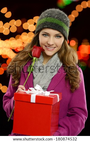 Young pretty girl with present and rose at night with lights on the background