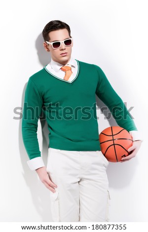 Retro basketball fashion man wearing white sunglasses a green sweater orange tie and white shorts. Studio shot against white wall.