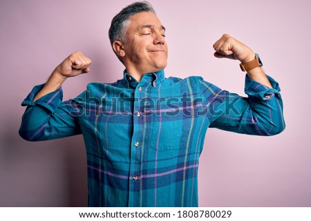Middle age handsome grey-haired man wearing casual shirt over isolated pink background showing arms muscles smiling proud. Fitness concept.